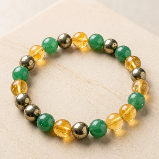 "A luxury 8mm natural gemstone Dhan Yog bracelet made of green aventurine, citrine, and pyrite beads, perfectly arranged in a round shape on a clean off-white stone surface with soft natural shadows."