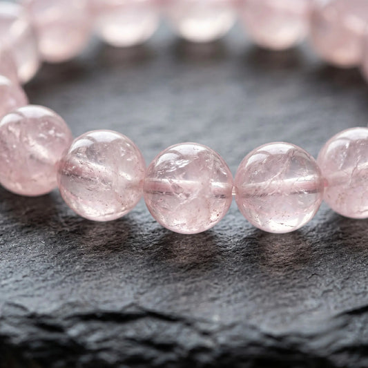 "Extreme macro close-up of a premium 8mm natural rose quartz bracelet, highlighting the authentic translucent pink color, inner clouds, and natural crystal textures resting on a dark slate surface."