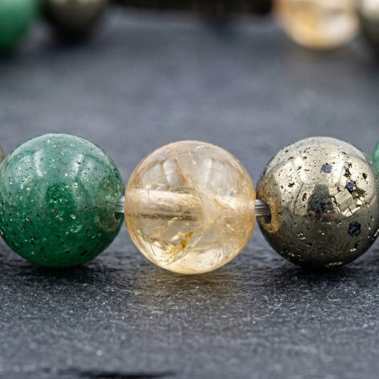 "Extreme macro close-up of a premium Dhan Yog crystal bracelet, showcasing the authentic natural textures, clarity, and metallic inclusions of 8mm green aventurine, citrine, and pyrite beads resting on a dark slate surface."