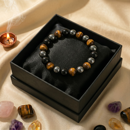 Premium 8mm Triple Protection crystal bracelet featuring authentic Tiger's Eye, Hematite, and Black Obsidian beads. The bracelet is elegantly displayed inside a luxurious matte black gift box resting on a golden silk background, surrounded by healing crystals and a glowing diya.