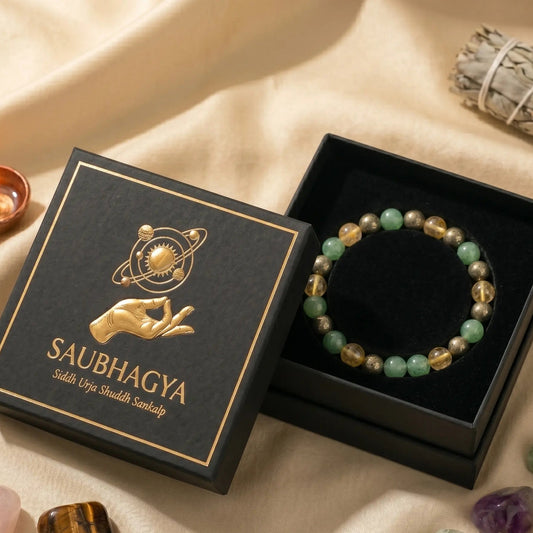 "Premium Dhan Yog crystal bracelet featuring 8mm pyrite, citrine, and green aventurine beads, elegantly resting on black foam inside a luxury gift box. The Saubhagya brand lid with a gold foil logo sits beside it on a silk cloth, surrounded by loose healing stones and a lit diya."